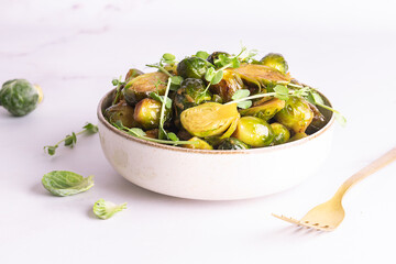 Tasty vegan low carb dish with fried Brussels sprout, peas greens and soy sauce on white marble background close up. Healthy diet food concept.
