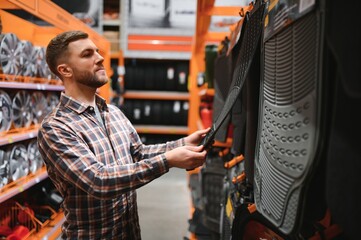 A man at the car shop or garage choosing floor carpets for his car from given examples
