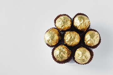 Chocolate candies — balls in golden wrappers and paper tartlets on a white table. Top view. Festive interior confectionery treat. Photo. Copy space