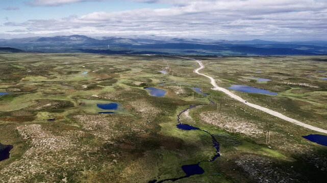 Aerial view, car driving on dirt road winding through tundra landscape. Camera zooms out to reveal the heathland and the ponds connected by streams, with mountains in the distance, J&auml;mtland Sweden