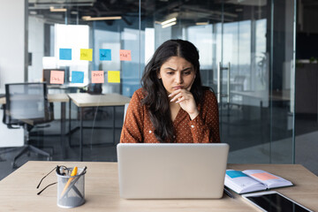 Serious thinking businesswoman at work with laptop inside office, female office worker prepares...
