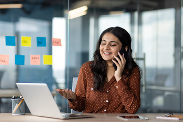 Young beautiful business woman talking on the mobile phone inside the office, the employee of...