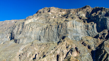 Breathtaking rock formations rise sharply in Colca Canyon, Peru, showcasing layered geology against a clear blue sky. This unique landscape attracts nature lovers and adventurers alike.