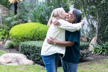 In garden, hugging and laughing, two senior multiracial female friends enjoying time together