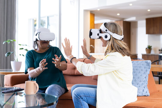At home, using vr headsets, two senior multiracial female friends interacting and having fun