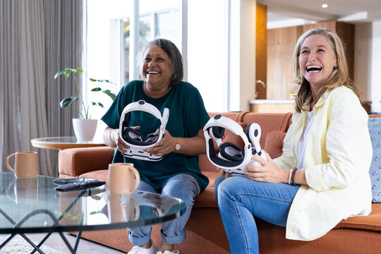At home, holding vr headsets, two senior multiracial female friends enjoying virtual reality gaming