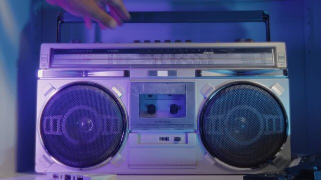 A Close-Up Of A Man Hand Sliding A Classic Cassette Into A Retro 80s Boombox, With Neon Lights Illuminating The Room, Bringing Back Nostalgic Vibes.