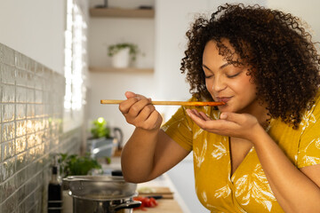 Tasting soup, woman with curly hair enjoying cooking in modern kitchen at home