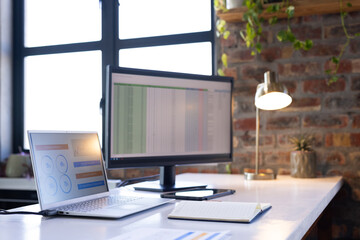 Working on business analytics, laptop and monitor displaying data in office
