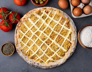 Chicken and Catupiry cream cheese pizza over stone background with flour, olives, tomatoes and eggs