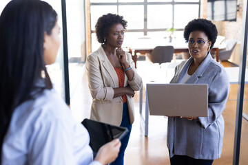 Discussing project, businesswomen using laptop and tablet in modern office setting