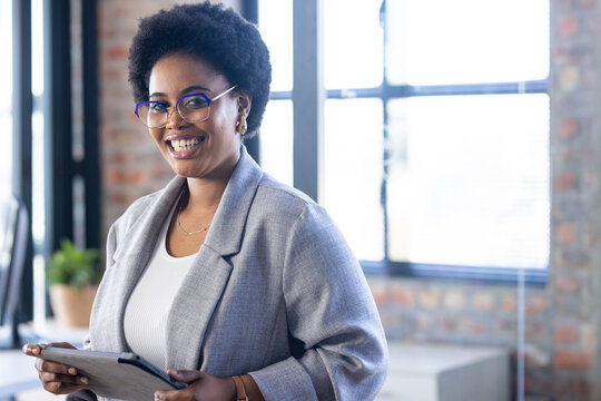 Holding tablet, businesswoman smiling confidently in modern office