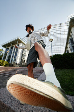 Vertical shot of teenage African American boy playfully kicking camera while having fun outside in city, fisheye effect, copy space