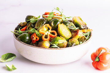 Tasty vegan low carb dish with fried Brussels sprout, peas greens, hot Habanero pepper and soy sauce on white marble background close up. Healthy diet food concept.
