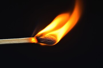 Close-up of a matchstick igniting with bright flames against a dark background