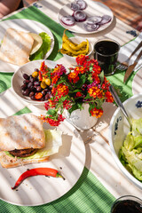 Ein gedeckter Tisch mit Tellern mit selbst gemachten Bürgern, vegan Ciabatta, Brötchen mit einem Blumenstrauß und Oliven und einer Salatschüssel