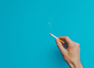 Naklejka premium A close up of hand holding cigarette against vibrant blue background, with wisps of smoke rising, creating striking visual contrast