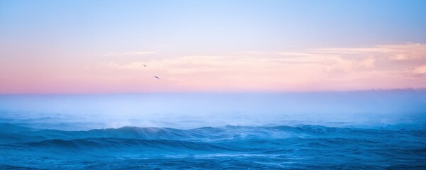Obraz premium Calm ocean waves under a pastel sky at sunset with distant seagulls flying over the water
