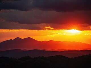 Stunning sunset over mountain range with dark clouds illuminated by vibrant orange and yellow hues during evening hours