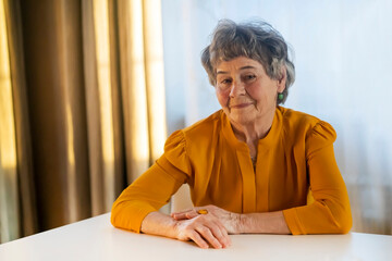 Old retired gray-haired woman in yellow blouse.