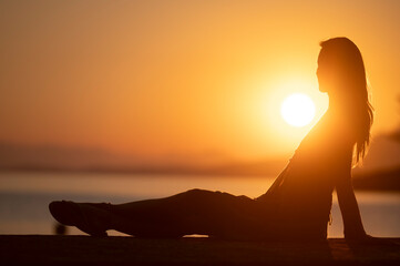 Profile view of a young woman sitting by the sea at beautiful sunrise