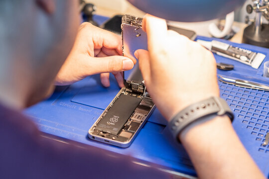 A technician carefully replaces a smartphone battery in a workshop, ensuring Quality and precision in the repair process