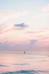 Man on a paddle board swimming in the sea at sunset