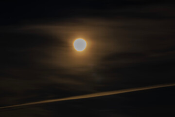 Obraz premium Close-up view of bright moon surrounded by thin clouds in dark night sky.