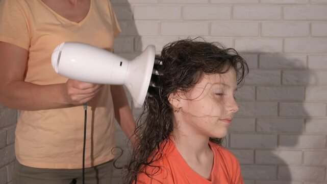 Female use hair dryer with daughter. A woman hand use hair styler and dry hair of her little daughter indoor.