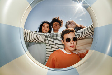 Fisheye shot of four teenagers posing together for camera holding swimming tube while enjoying...