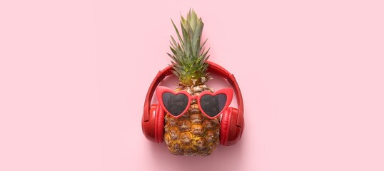 Fresh pineapples with sunglasses and headphones on pink background