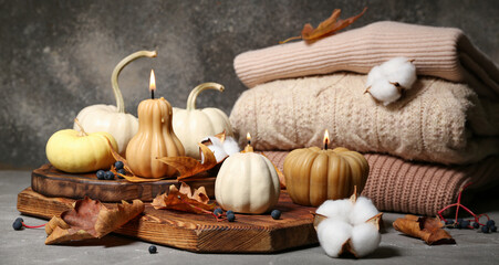 Beautiful composition with burning candles in shape of pumpkin, cotton flowers and autumn leaves on grey background