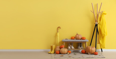 Hanger with raincoat and bench with boots, umbrella and pumpkins with autumn leaves in interior of hallway