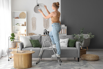 Young woman on stepladder screwing light bulb into hanging lamp at home