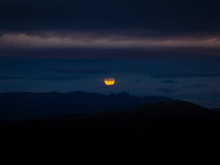 Luna Llena que asoma entre nubes sobre el horizonte