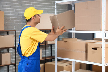 Delivery man taking parcel box from shelf in warehouse