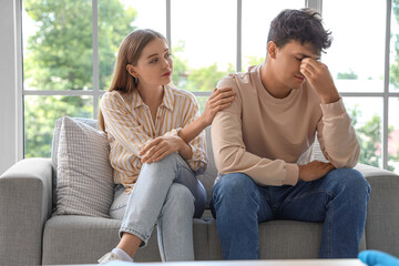 Obraz premium Young woman with her upset husband sitting on sofa at sexologist's office