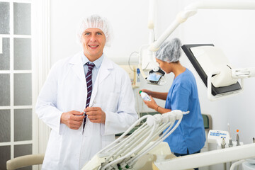Obraz premium Positive male dentist standing in dental office looking at the camera