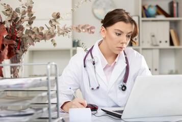 Portrait of female doctor who is working with laptop and documents in clinic