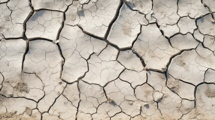 A close-up of dry, cracked earth. The cracks are deep and wide, and the earth is a light brown color. The texture is rough and uneven.