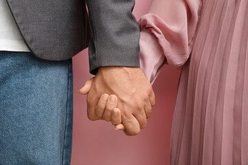 Couple holding hands on pink background, closeup