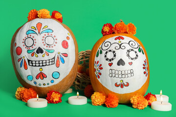 Pumpkins with painted skulls, marigolds and burning candles on green background. El Dia de Muertos