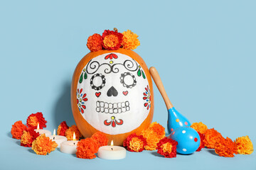 Pumpkin with painted skull, maracas, burning candles and flowers on color background. El Dia de...