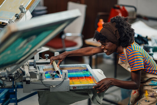 Happy female diverse worker silkscreen printing on machine at workshop