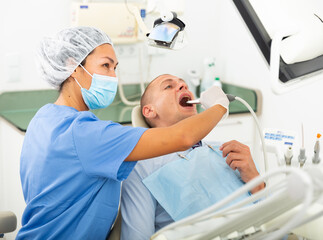 Fototapeta premium Qualified woman dentist in a protective mask working in the clinic conducts an examination of a man patient sitting in a ..dental chair using an apexlocator