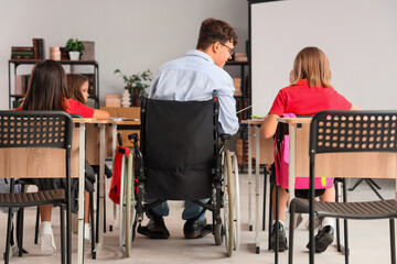 Male teacher in wheelchair conducting to little pupils at school, back view