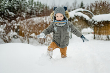 Adorable little boy having fun on snowy winter day. Cute child wearing warm clothes playing in a snow.