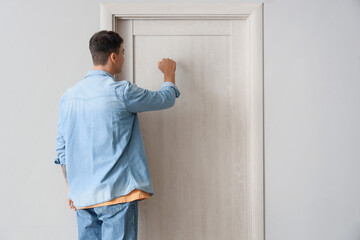 Young man knocking on door in hall, back view