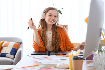 Female web designer with headphones and graphic tablet working at table in office