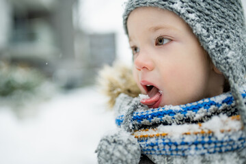 Adorable little boy having fun in a city on snowy winter day. Cute child wearing warm clothes playing in a snow.